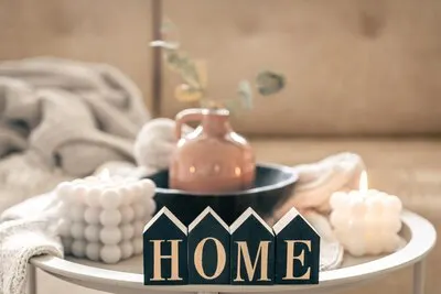 Cozy composition with decorative word home candles and vase on blurred background