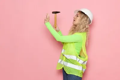 Front view young female builder in green construction suit white helmet using a hammer on the pink space job architecture construction job
