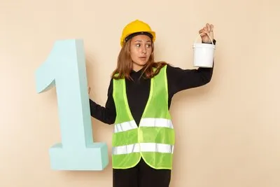 Front view female builder in yellow helmet holding paint and number one figure on the white wall