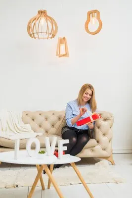 Young happy lady with gift box on sofa near table with love sign