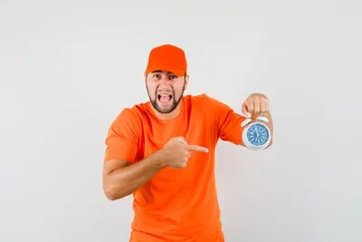 Delivery man pointing at alarm clock while screaming in orange t-shirt, cap and looking agitated , front view.