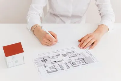 Midsection of woman working on house blueprint at desk in office