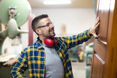 Professional blonde middle aged carpenter checking quality of wood product in his carpentry workshop