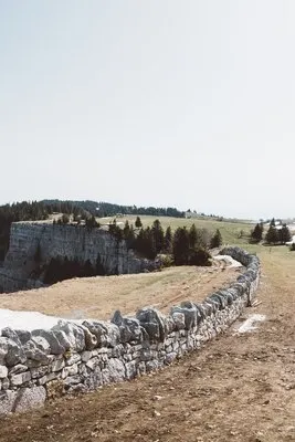 Stone wall near a cliff on a green field under a cloudy sky