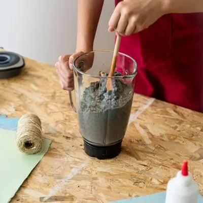 Close-up of a woman's hand stirring paper pulp in blender over desk