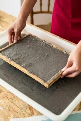 Woman's hand holding mold with pulp for making paper