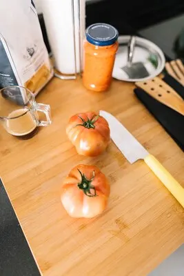 Two red tomatoes on chopping board with sharp knife