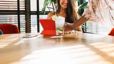 Female waitress serving cocktail to female customer on wooden table