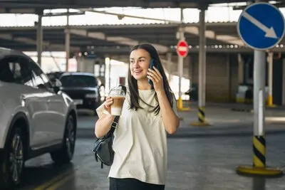 A young woman with coffee talking on the phone in the parking lot