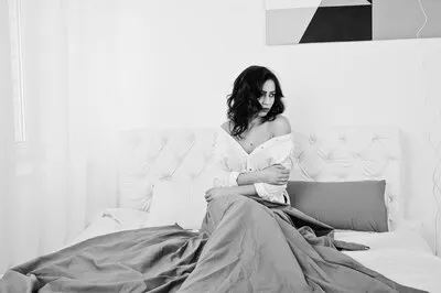 Studio portrait of brunette girl in white blouse lying on bed