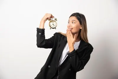Business woman looking on an alarm clock on white wall.