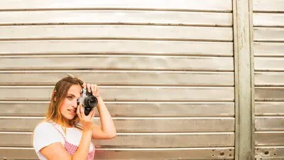 Smiling young woman standing in front of shutter door taking photo with camera