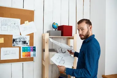 Young successful architector smiling, holding drawings, standing in office