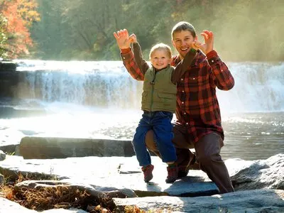 Smiling father with his son in a park surrounded by greenery and a waterfall under the sunlight