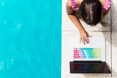 Young female browsing laptop on edge of pool