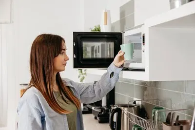 Casual girl using microwave to heat cup