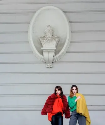 Fashion models in yellow and red fur coats pose before a white wall