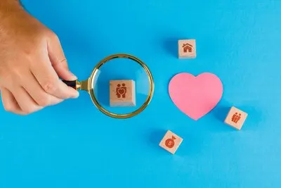 Family concept with paper cut heart on blue table flat lay. hand holding magnifying glass over wooden cube.