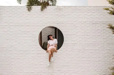 Stunning young woman sitting on bricked wall Outdoor shot of adorable girl in sunglasses posing on urban background