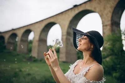 Woman in hat by railroad bridge with dandelion