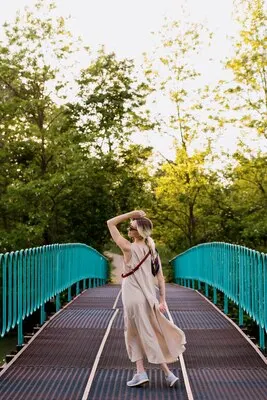 Beautiful relaxed blonde young woman wearing dress, posing in motion on the bridge.