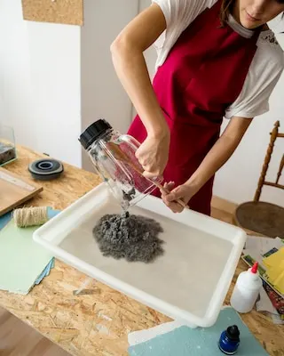 Woman putting grinded paper pulp in water over wooden desk