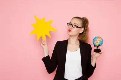 Front view of female office worker in black strict jacket holding a big yellow sign with globe on pink wall