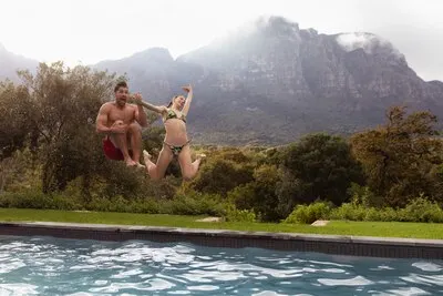 Couple jumping together in the swimming pool at backyard