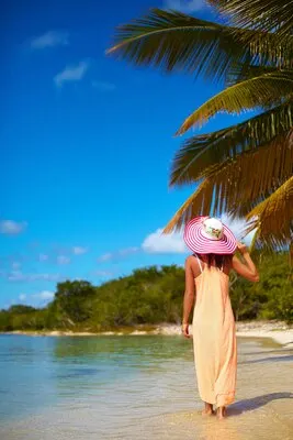 Hot beautiful woman in colorful sunhat and dress walking near beach ocean on hot summer day near palm