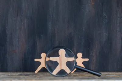 Marketing analysis concept with magnifying glass over wooden figure on wooden and grunge background side view.
