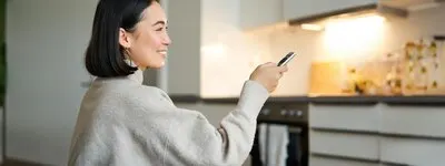 Close up portrait of smiling asian woman watching television sitting on sofa with remote and