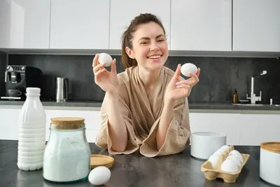 Attractive young cheerful girl baking at the kitchen making dough holding recipe book having ideas