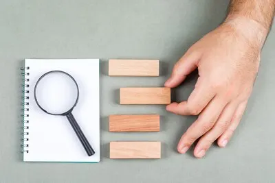 Research and search results concept with notebook, magnifier, wooden blocks on gray background top view. hand picking one of the results. horizontal image