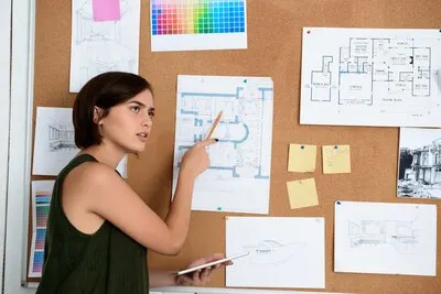 Young beautiful businesswoman standing near desk with drawings