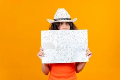 A surprised young woman with short hair in an orange shirt wearing sun hat looking through map