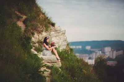 Lady with red bouquet sits on green hill