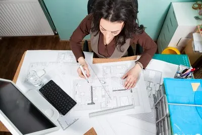 Top view of architect working at her desk with blueprints in front of her. Working on new projects. Architecture and design