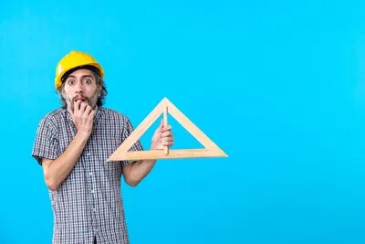 Front view male builder in helmet holding triangle wooden figure on blue background constructor design engineer architecture building color