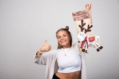 Blonde woman giving thumbs up with Christmas stocking on gray background.