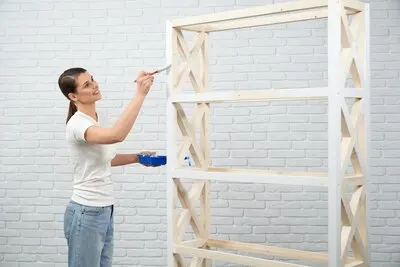 Smiling woman painting in white color wooden shelves