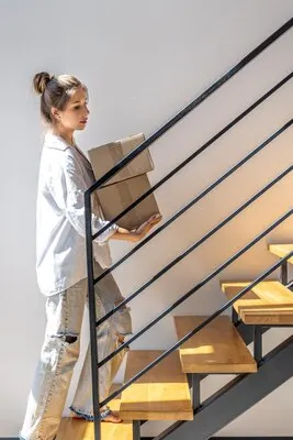 Young woman with parcels going up modern wooden stairs upward motion