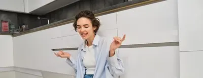 Candid smiling young woman sits on floor at home works remotely connects to online group chat