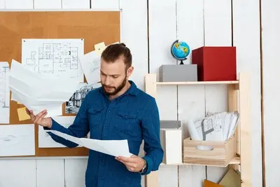 Young successful architector looking at drawings, standing in office