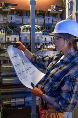 Woman electrician reads blueprint to set up switchgear pre launch plan