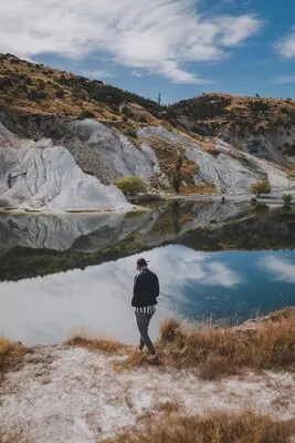 Vertical shot of a man walking near Blue Lake Walk in New Zealand surrounded by mountains