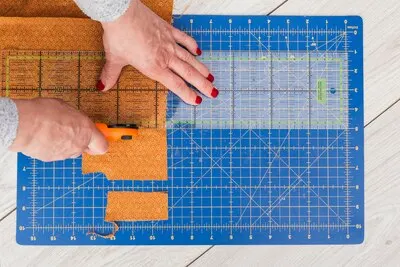 An overhead view of a woman's hand cutting fabric to smaller part with rotary cutter on wooden table