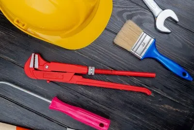 Top view of pattern from set of construction tools as screwdriver pipe wrench safety helmet paint brush and open-end wrench on wooden background