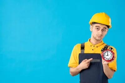 Front view of serious male worker in yellow uniform with clocks on blue