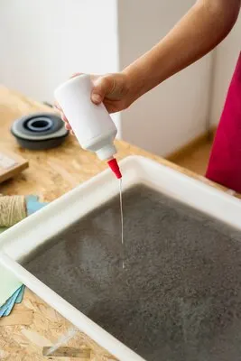 Woman's hand pouring glue in pulp for making paper