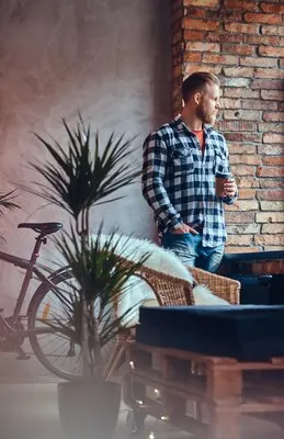 The full body image of blond hipster male drinks coffee in a room with loft interior.